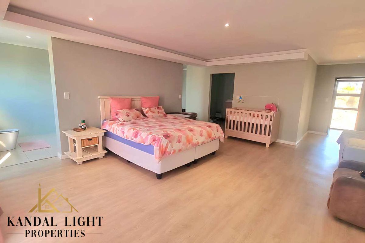 Spacious bedroom featuring light wood-look flooring, recessed ceiling lighting, and an open-plan layout with an integrated en-suite bathroom area.