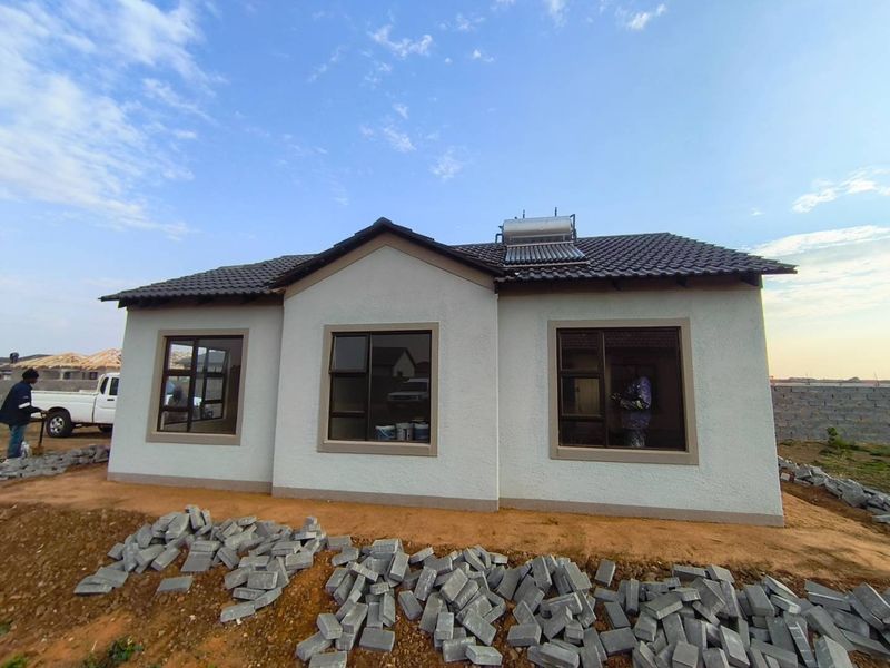 Front view of a newly constructed single-story house featuring a tiled roof, solar water heater, and modern aluminium window frames.