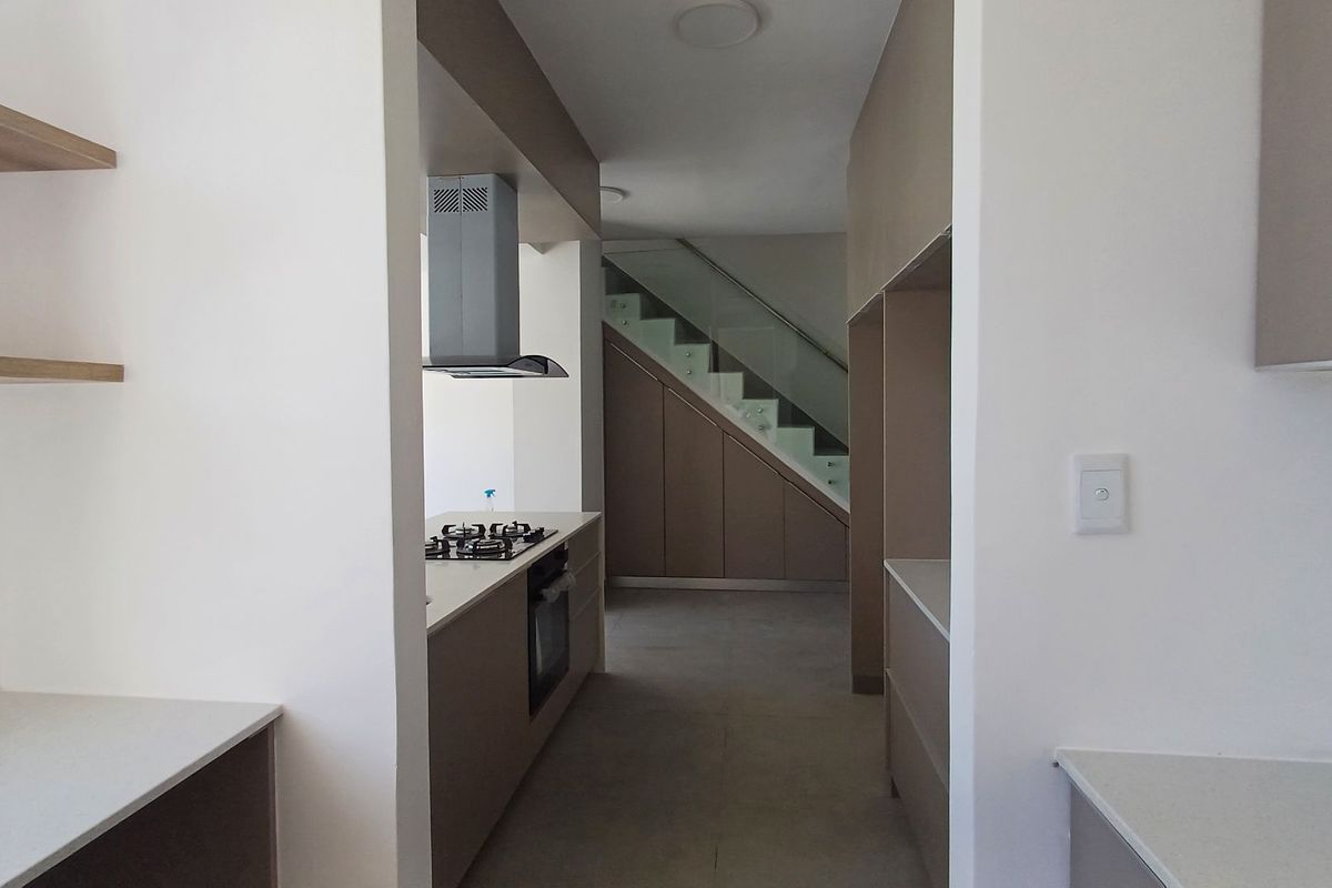 Modern kitchen featuring sleek cabinetry, stone countertops, integrated gas hob and oven, with an adjacent staircase and under-stair storage.