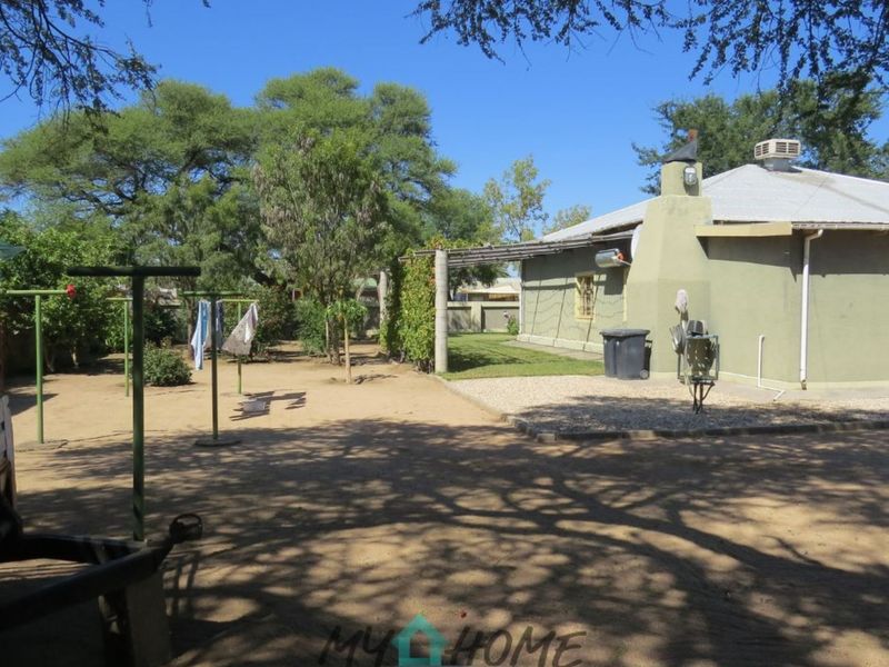 Spacious rear garden area featuring a paved patio section, outdoor fireplace, and established trees, providing a functional outdoor space for the property.