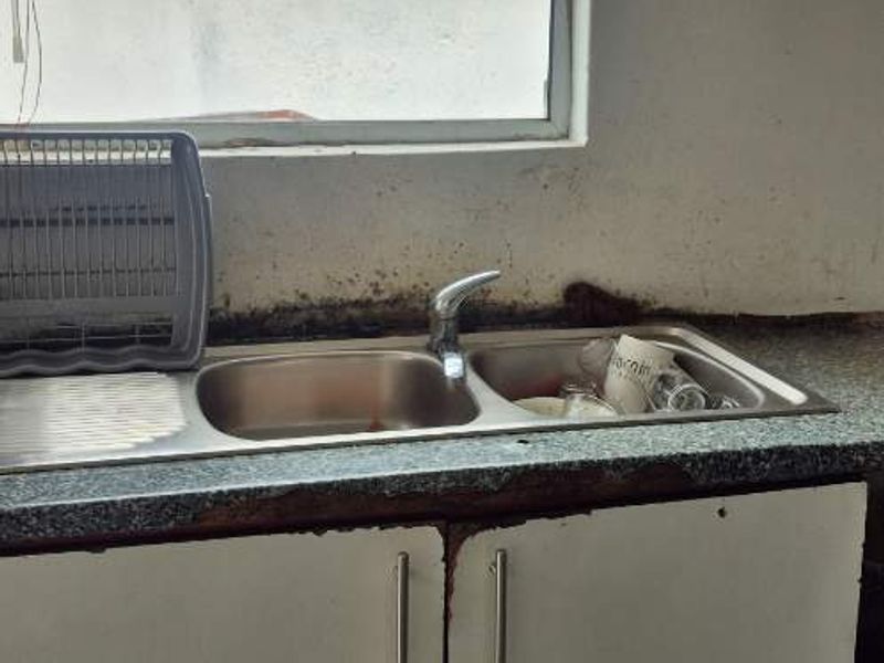 A kitchen sink area featuring a stainless steel basin and base cabinetry, showing significant signs of water damage and wear to the fixed finishes.