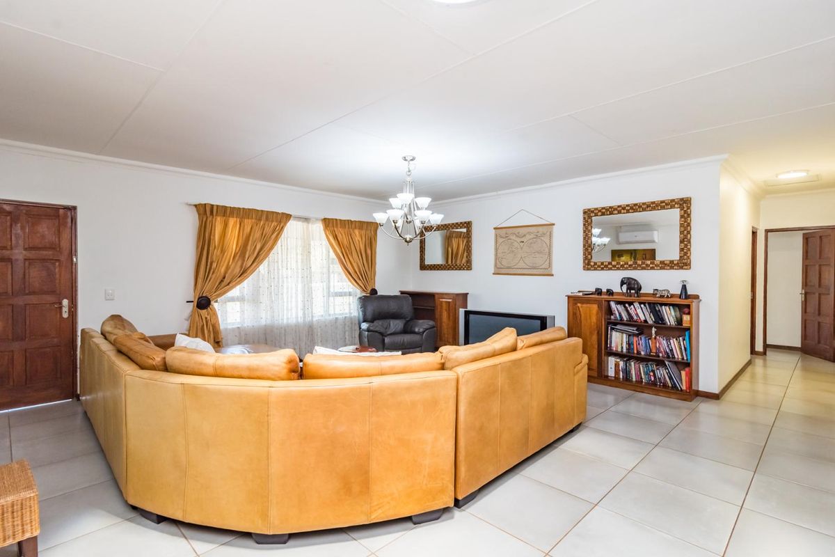 Spacious living room featuring neutral floor tiles, a central chandelier, and direct access to adjacent rooms through wooden doors.