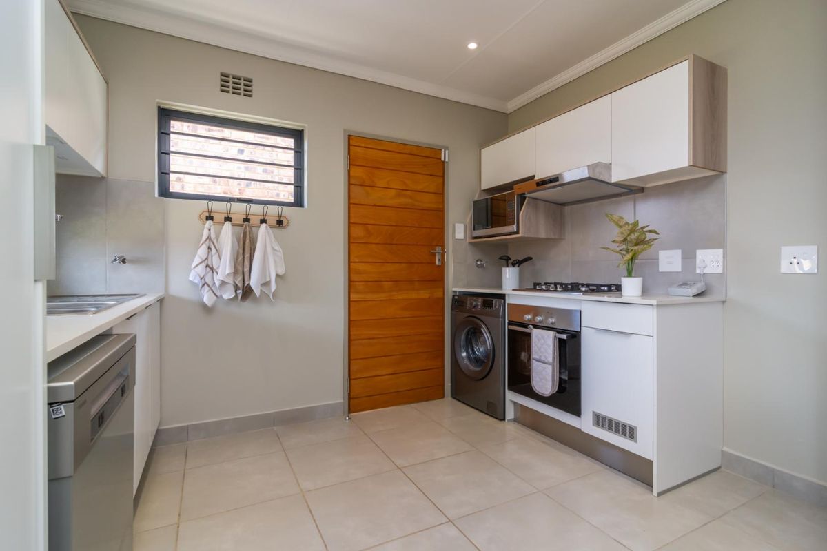 Modern kitchen featuring built-in cabinetry, gas hob, electric oven, extractor fan, built-in microwave, and tiled flooring with a timber door.