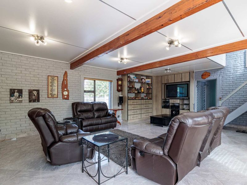 Spacious living room featuring exposed timber ceiling beams, a painted brick feature wall, and built-in cabinetry with integrated shelving.