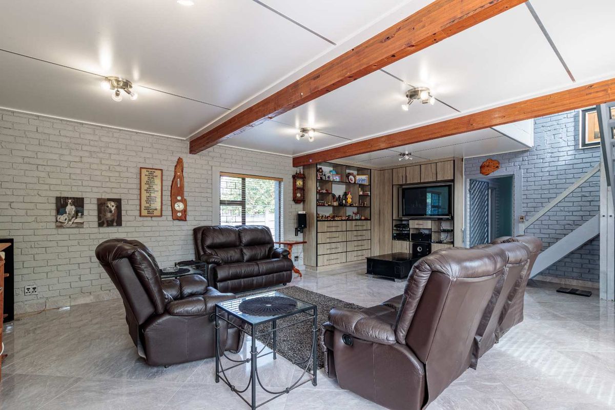 Spacious living room featuring exposed timber ceiling beams, a painted brick feature wall, and built-in cabinetry with integrated shelving.