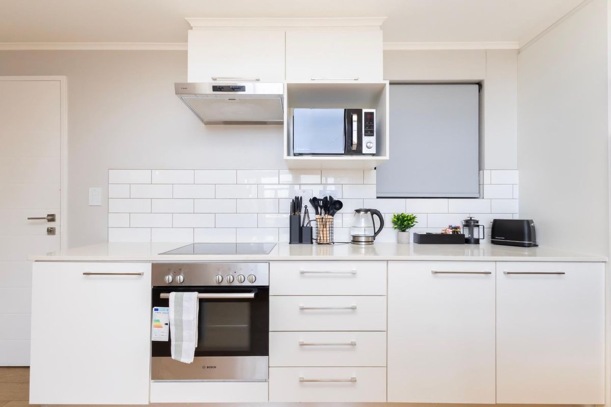 Modern kitchen featuring white cabinetry, quartz countertops, subway tile backsplash, and integrated stainless steel appliances including an oven, hob, and extractor fan.