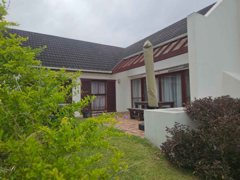 Rear view of the property featuring a paved patio area, built-in braai, and direct access to the interior through sliding glass doors.