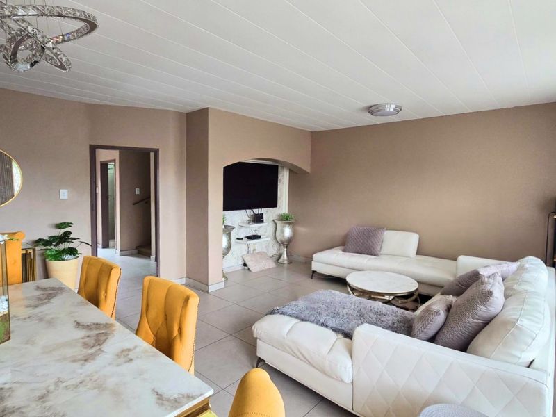 Spacious open-plan living and dining area featuring tiled flooring, a recessed television alcove, and a modern ceiling light fixture.