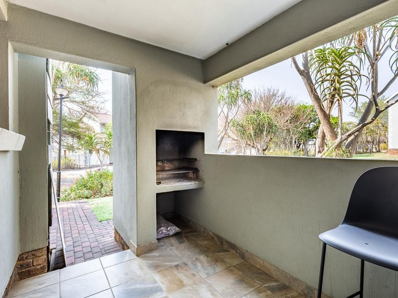 A covered patio area featuring a built-in braai and tiled flooring, offering a functional outdoor space for entertaining.