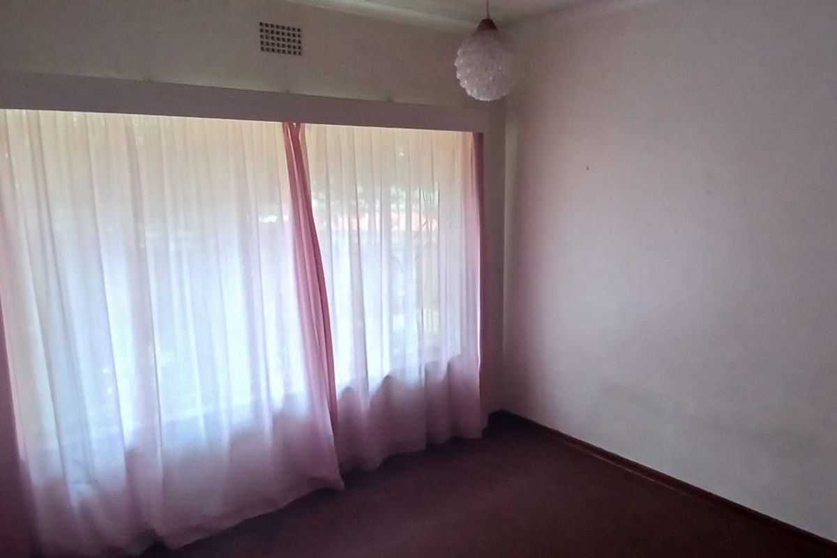 A vacant bedroom featuring a large window with sheer curtains, carpeted flooring, and a central ceiling light fixture.