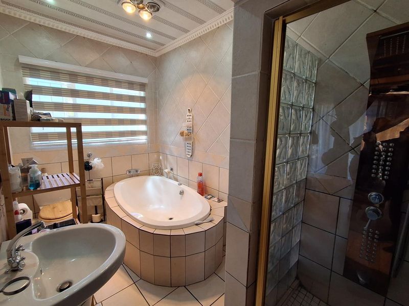 A functional bathroom featuring a built-in bathtub, a separate shower enclosure with glass block detailing, and tiled finishes throughout.