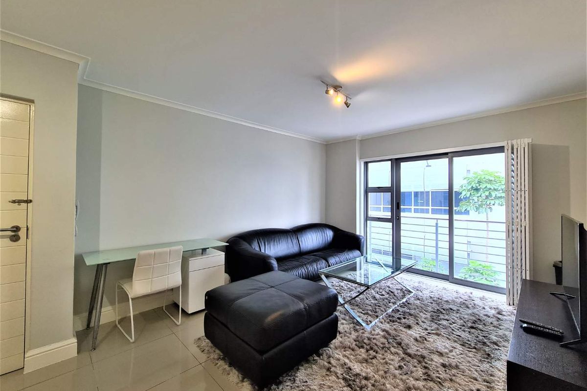 A bright living room featuring tiled flooring, neutral walls, and large sliding glass doors that open onto a balcony.