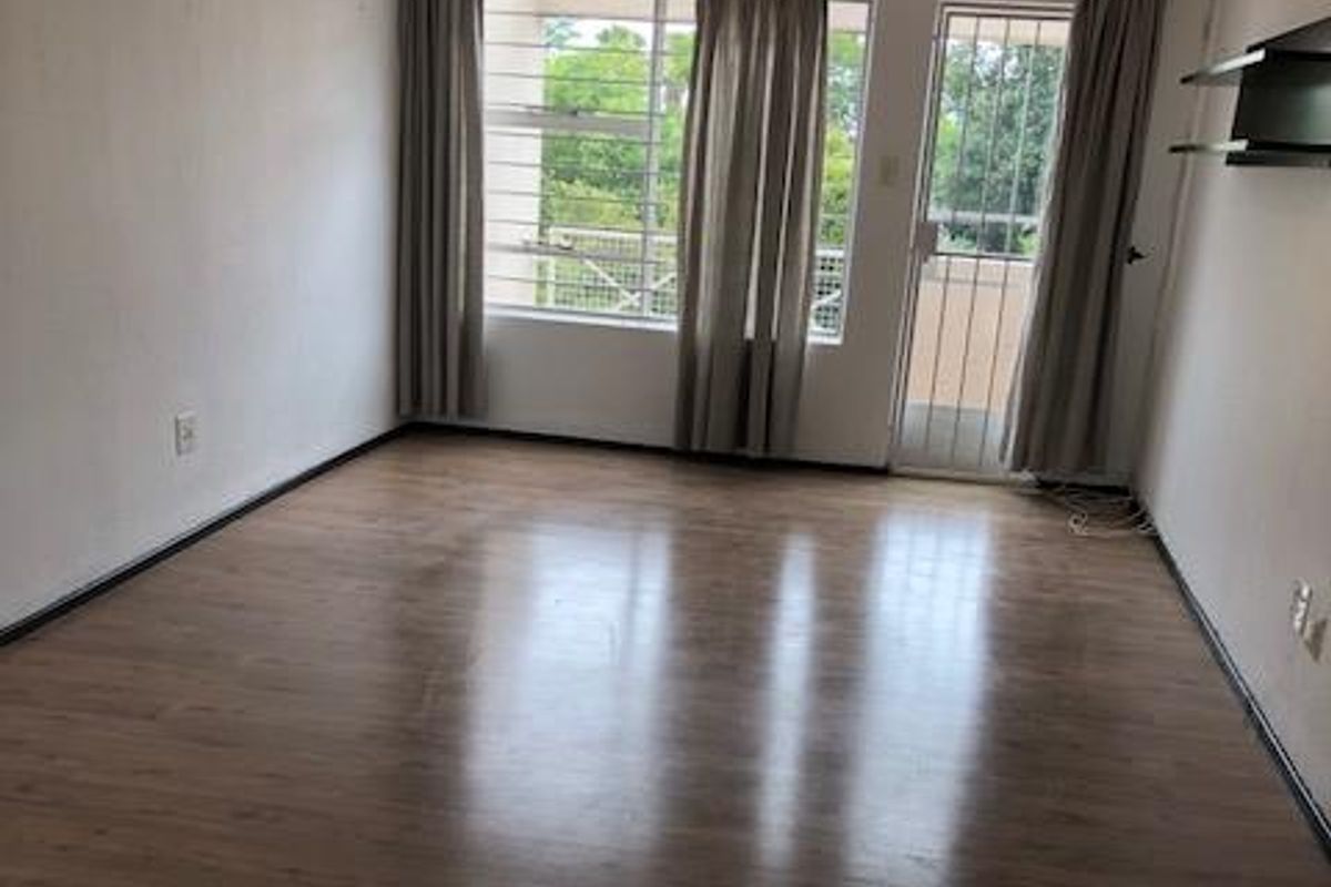 A bright, empty living room featuring wood-look laminate flooring, large windows with security bars, and direct access to an outdoor balcony area.