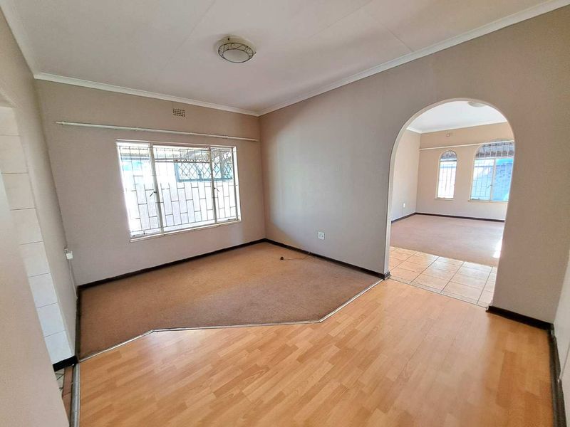An empty living area featuring an arched transition to an adjacent room, with a mix of laminate and carpeted flooring and security bars on windows.
