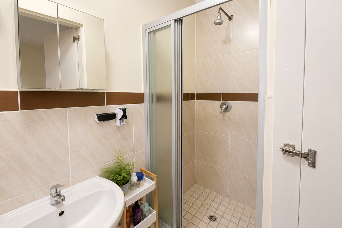 A functional bathroom featuring a tiled shower enclosure, pedestal basin with mixer tap, and a wall-mounted mirrored vanity cabinet.