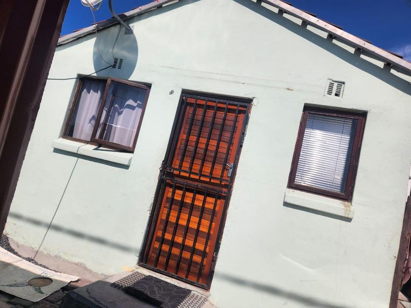 Front facade of the house featuring a timber entrance door with a security gate and two windows with dark frames.