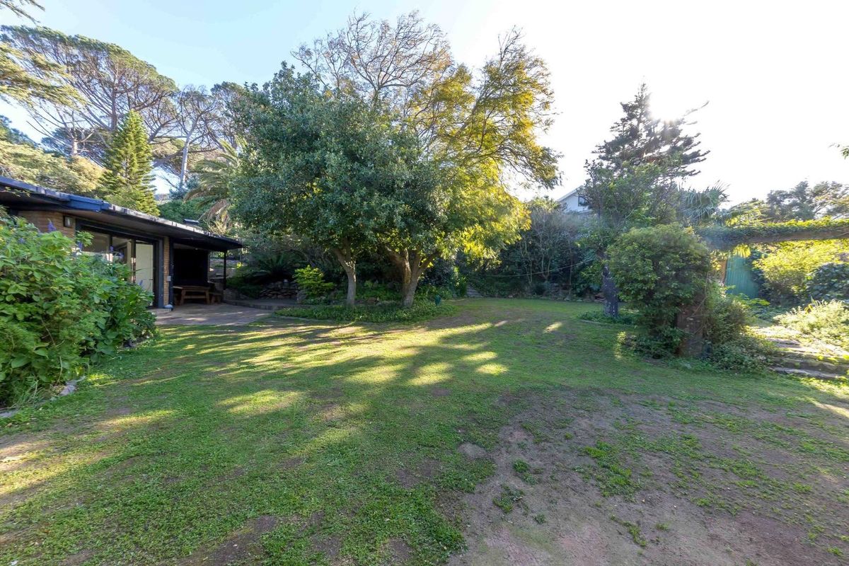 A spacious rear garden featuring a large lawn, mature trees, and a paved patio area adjacent to the house.