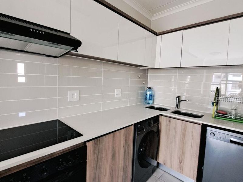 Modern kitchen featuring sleek white and wood-grain cabinetry, stone countertops, integrated oven and hob, and a tiled backsplash with contemporary finishes.