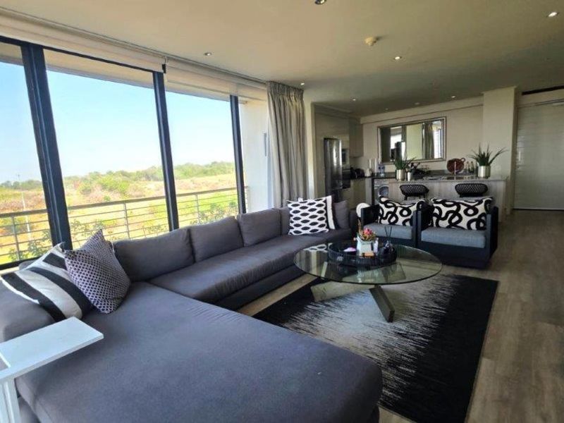 Modern open-plan living area featuring floor-to-ceiling windows, recessed lighting, and seamless flow to the kitchen and balcony.