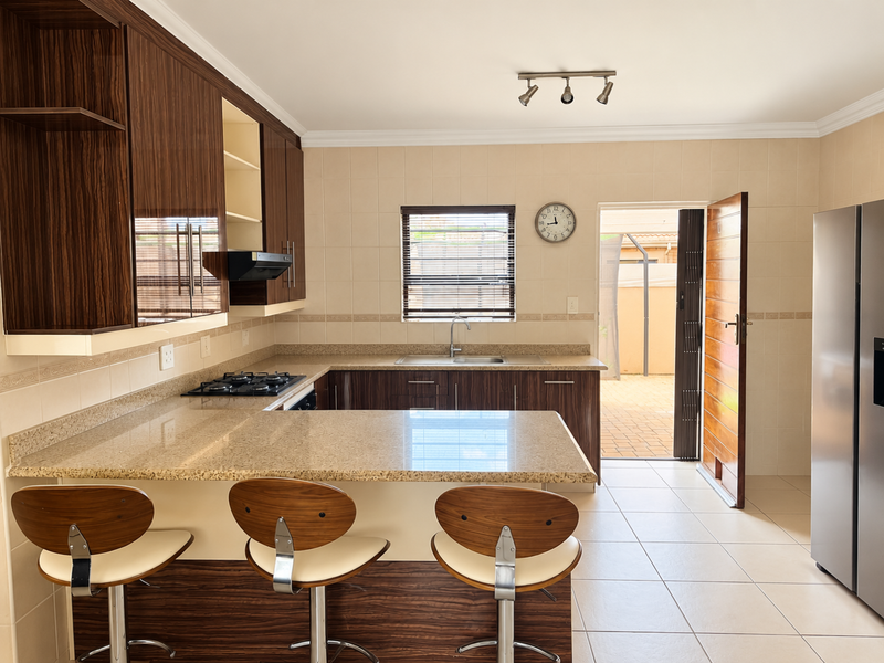 A well-maintained kitchen featuring granite countertops, dark wood cabinetry, a gas hob with extractor, and direct access to an outdoor patio area.