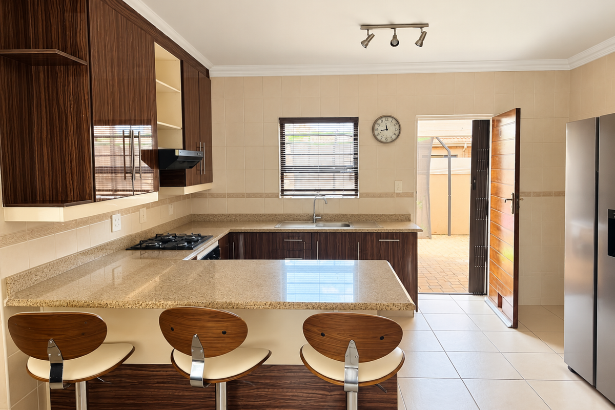 A well-maintained kitchen featuring granite countertops, dark wood cabinetry, a gas hob with extractor, and direct access to an outdoor patio area.