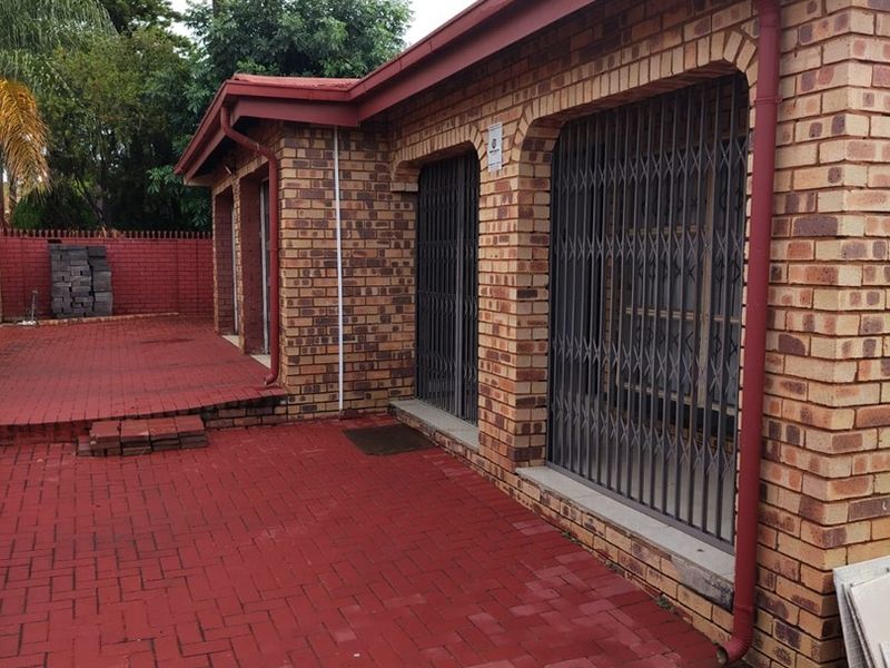 Rear exterior view of a face brick house featuring a paved patio area and security gates on the windows.