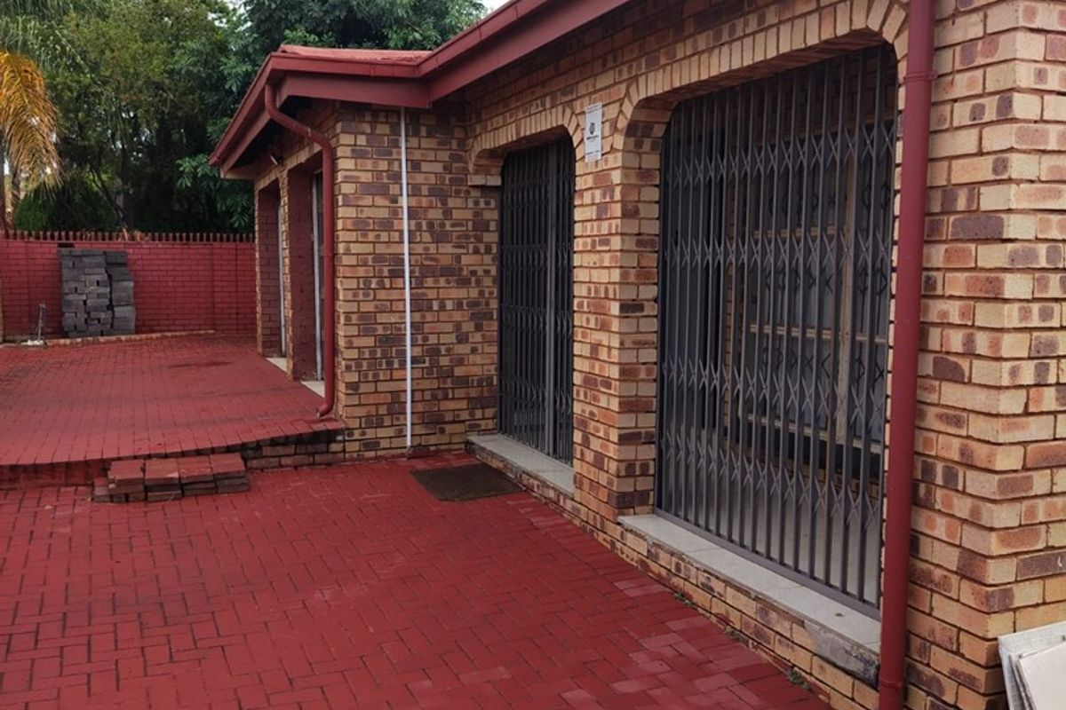 Rear exterior view of a face brick house featuring a paved patio area and security gates on the windows.