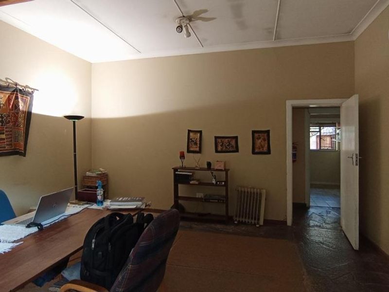 A functional office space featuring stone flooring and an exposed ceiling beam, providing a practical work environment with access to an adjoining room.