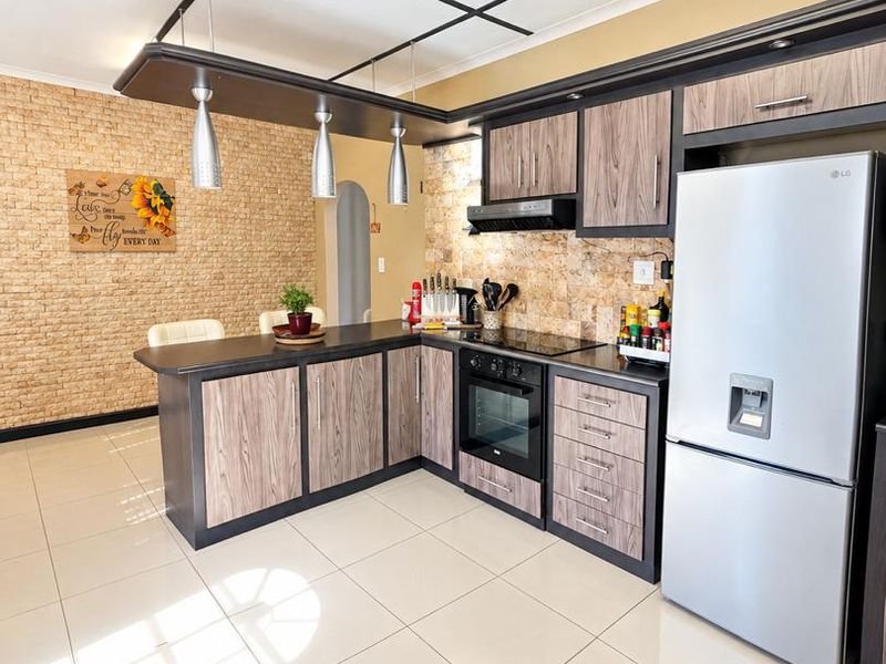 Modern kitchen featuring wood-grain cabinetry, stone-look feature wall, breakfast bar, and integrated appliances with neutral tiled flooring.
