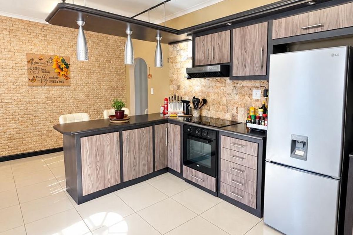 Modern kitchen featuring wood-grain cabinetry, stone-look feature wall, breakfast bar, and integrated appliances with neutral tiled flooring.