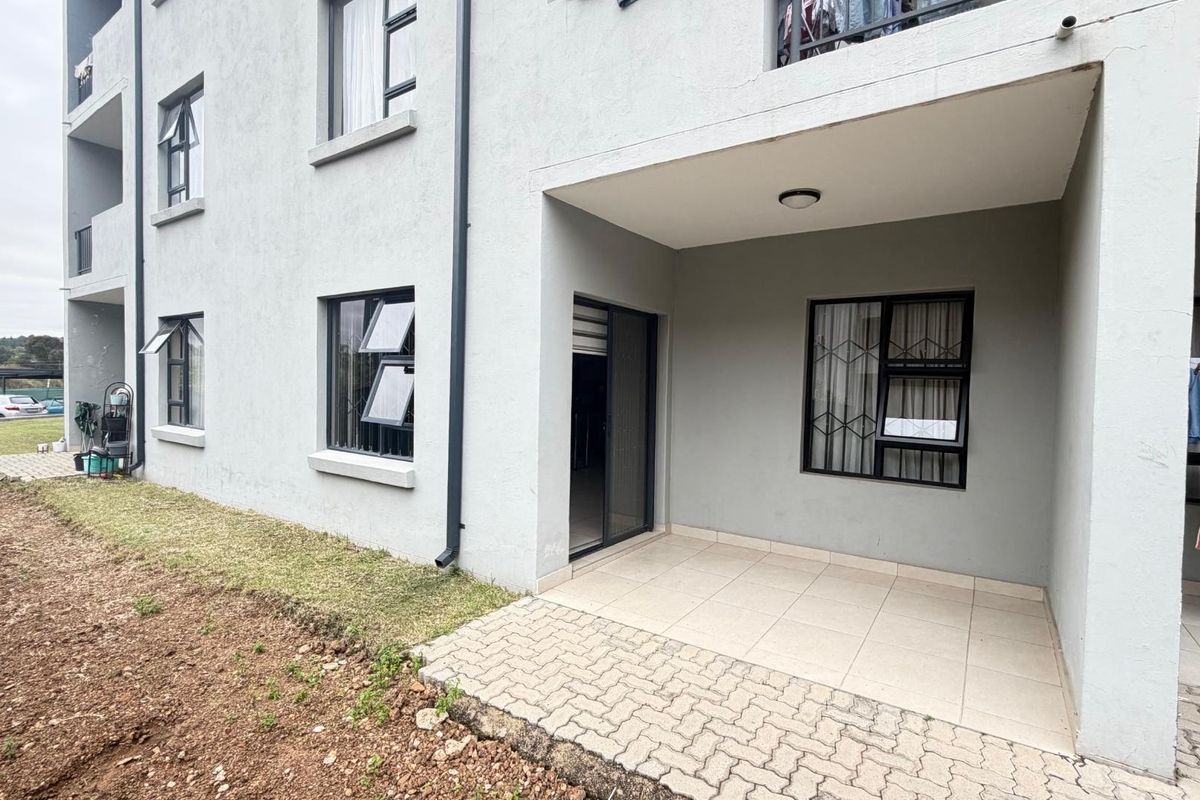 Exterior view of an apartment building featuring a ground-floor patio with tiled flooring and security bars on the windows.