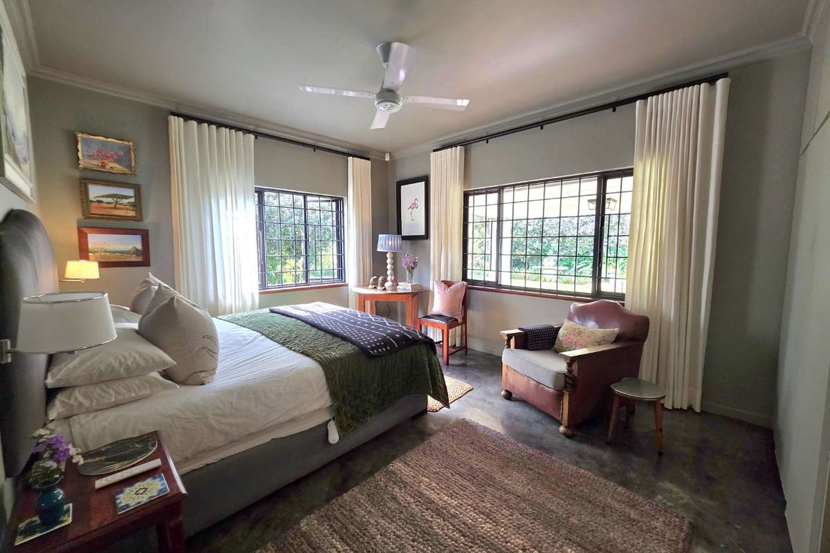 A well-lit bedroom featuring polished concrete flooring, large windows with security bars, and a ceiling fan.