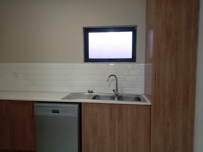 A clean, modern kitchen area featuring wood-finish cabinetry, a double bowl sink with mixer tap, and a classic white subway tile backsplash.