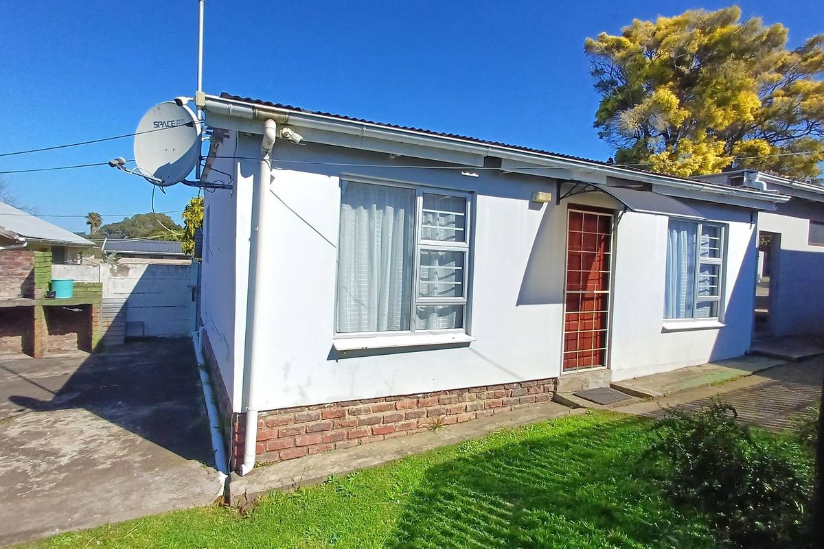 Rear exterior view of the property featuring a brick base, security gate, and a built-in outdoor braai area.