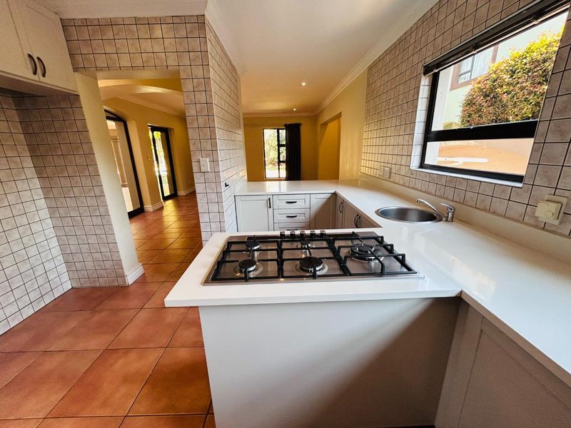 A functional kitchen featuring a gas hob, tiled splashbacks, and built-in cabinetry, leading into an open-plan living area with tiled floors.