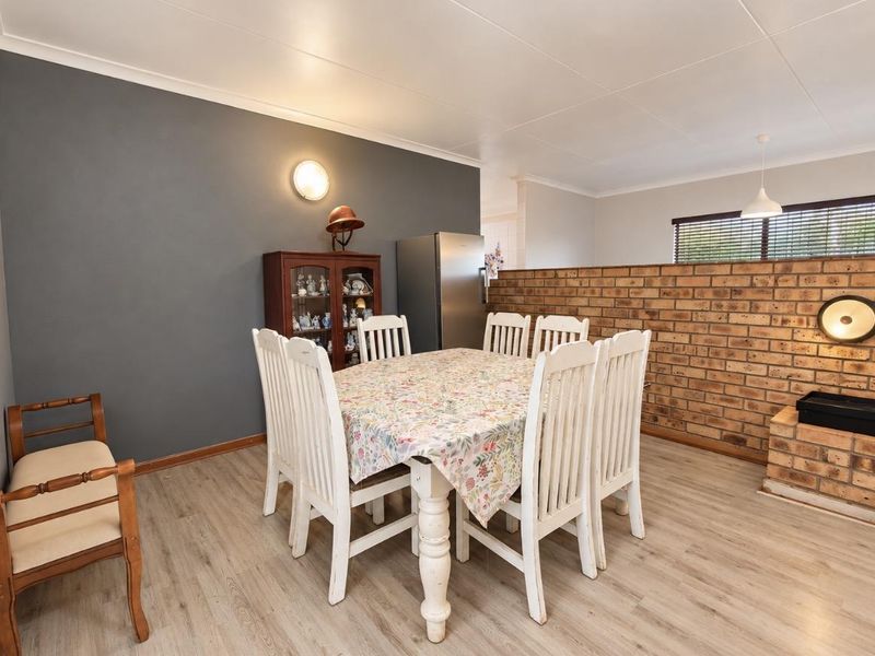 Dining area featuring a brick feature wall, laminate flooring, and an integrated brick fireplace, creating a warm and rustic atmosphere.