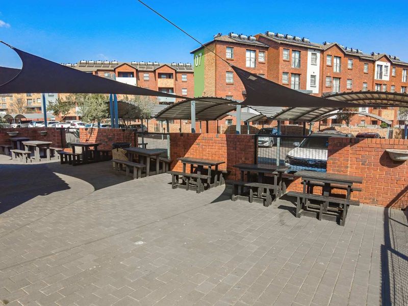 Outdoor communal entertainment area featuring paved flooring, brick boundary walls, and overhead shade sails within an apartment complex.