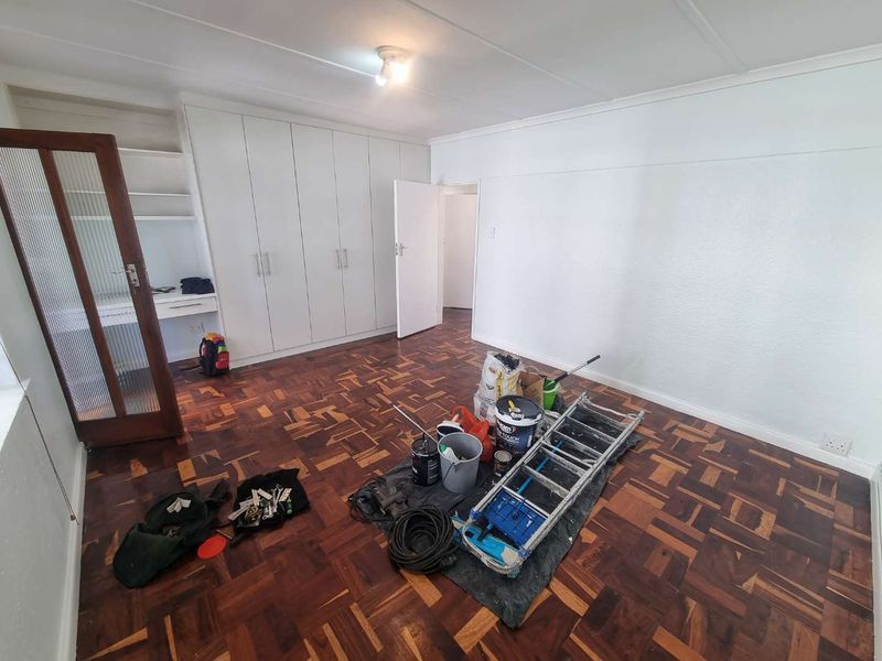 A spacious bedroom featuring classic parquet flooring and extensive built-in cupboard storage, currently undergoing minor maintenance and painting.