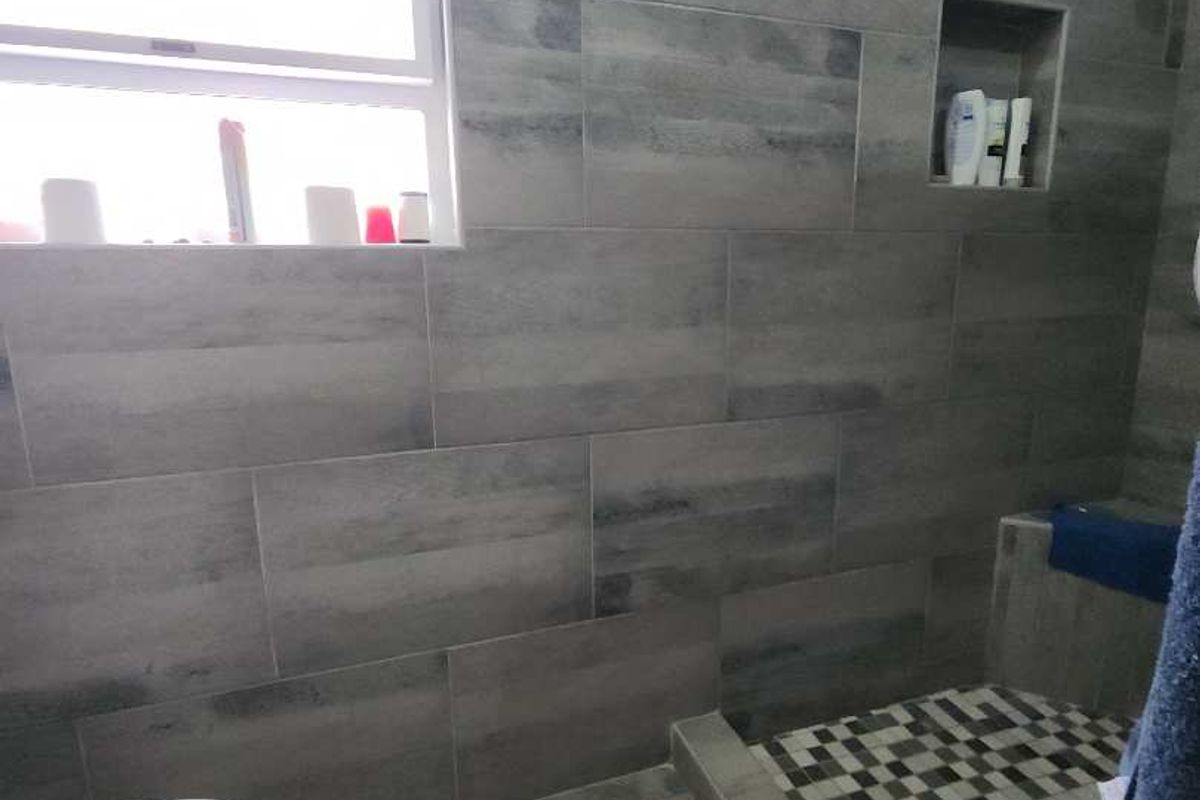 Modern bathroom featuring grey wall tiles, a walk-in shower with mosaic floor tiling, a built-in shower niche, and a window for natural light.