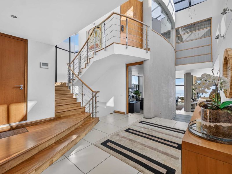 Spacious double-volume entrance hall featuring a timber staircase with stainless steel balustrades, tiled flooring, and a large skylight providing abundant natural light.