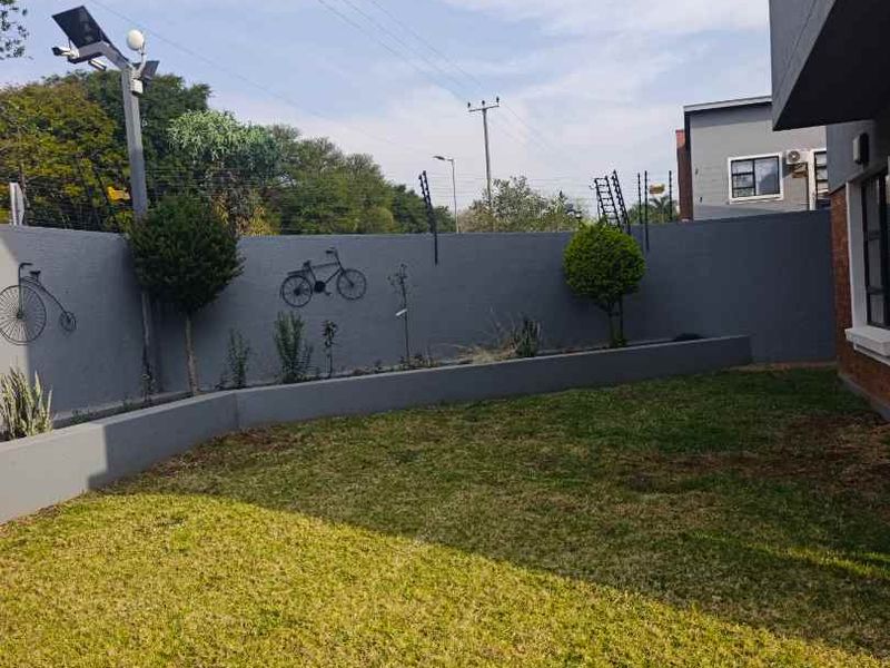 A private rear garden featuring a well-maintained lawn, raised garden beds, and a secure perimeter wall equipped with electric fencing.