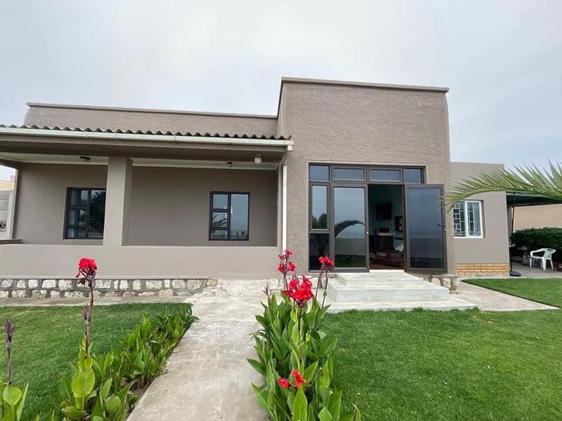 Rear view of the house featuring a covered patio, stone-clad foundation, and modern aluminium-framed glass doors leading into the living area.