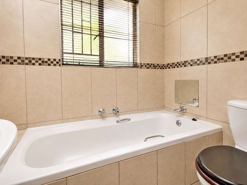A well-maintained bathroom featuring a built-in bathtub, pedestal basin, toilet, and neutral ceramic wall tiles with a decorative mosaic border.