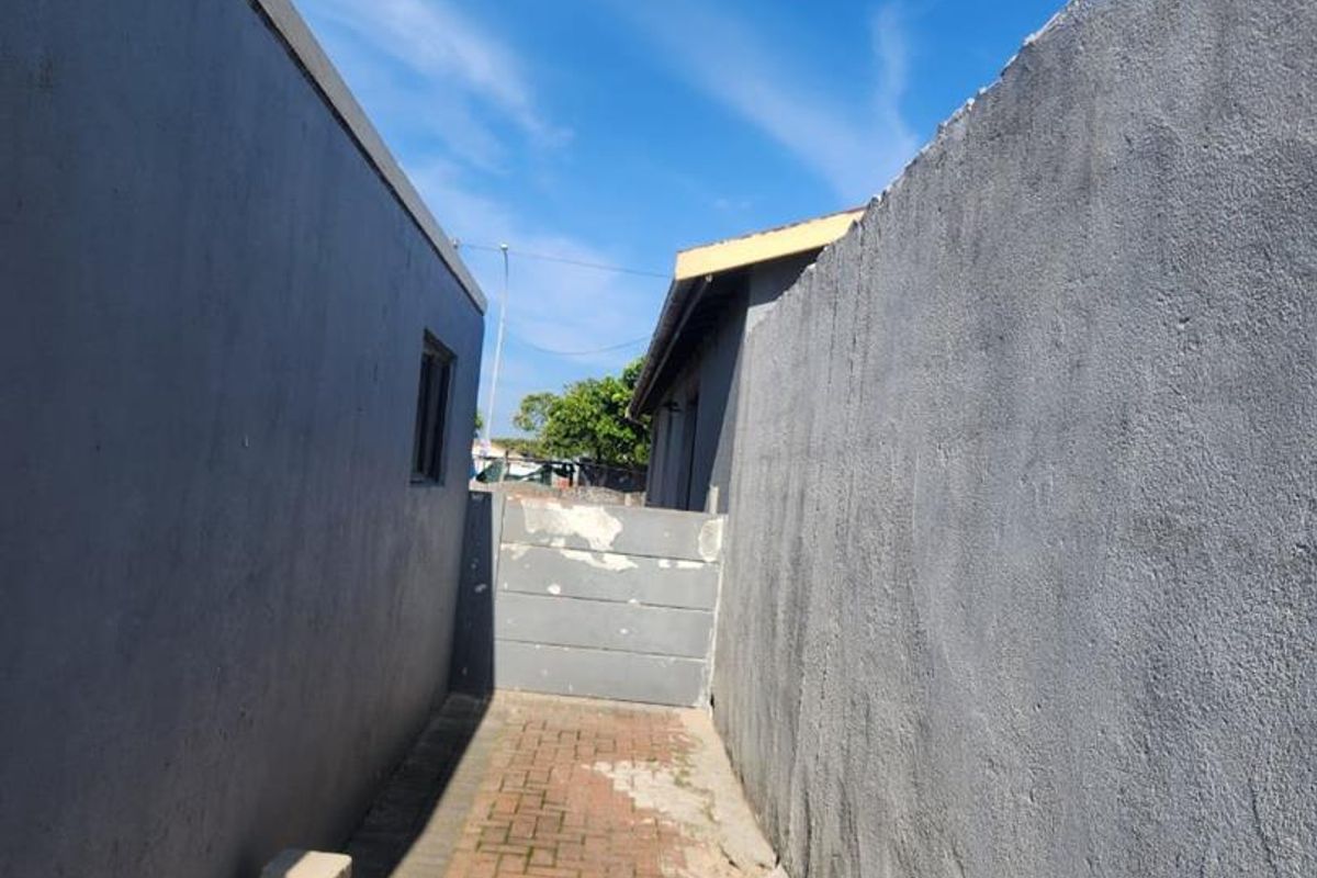 A narrow side passage between two structures featuring paved flooring and high boundary walls.