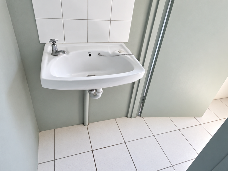 A clean, functional bathroom area featuring a wall-mounted basin with a tiled splashback and neutral floor tiling.