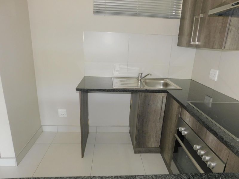 Compact kitchen featuring granite countertops, built-in oven, electric hob, extractor fan, and tiled finishes. Includes a dedicated space for an under-counter appliance.