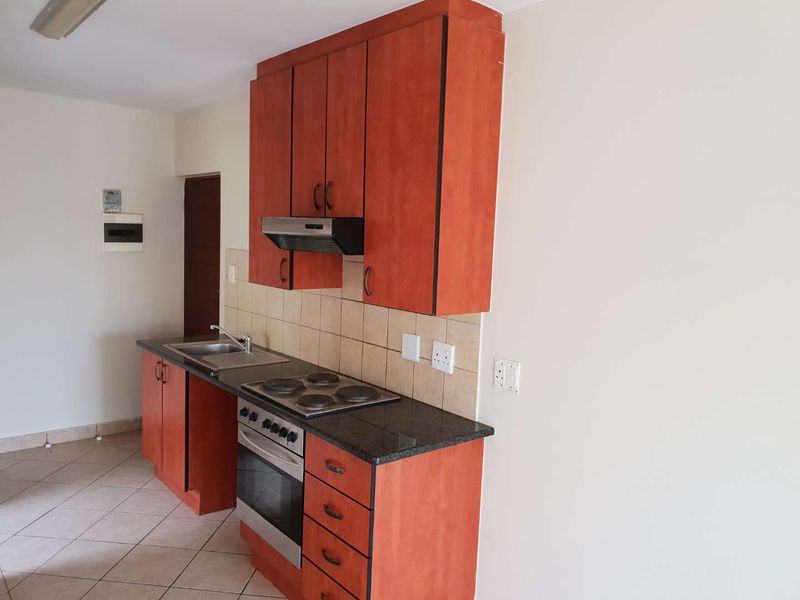 A compact kitchen featuring wooden cabinetry, granite countertops, a built-in oven with hob, and a tiled backsplash.