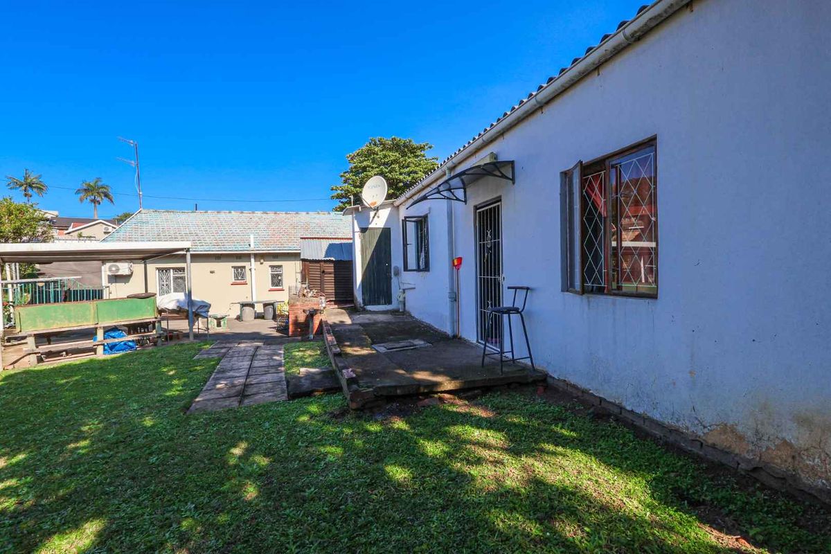 Rear exterior view of the property featuring a concrete patio area, lawn, and access to the main dwelling and outbuilding.
