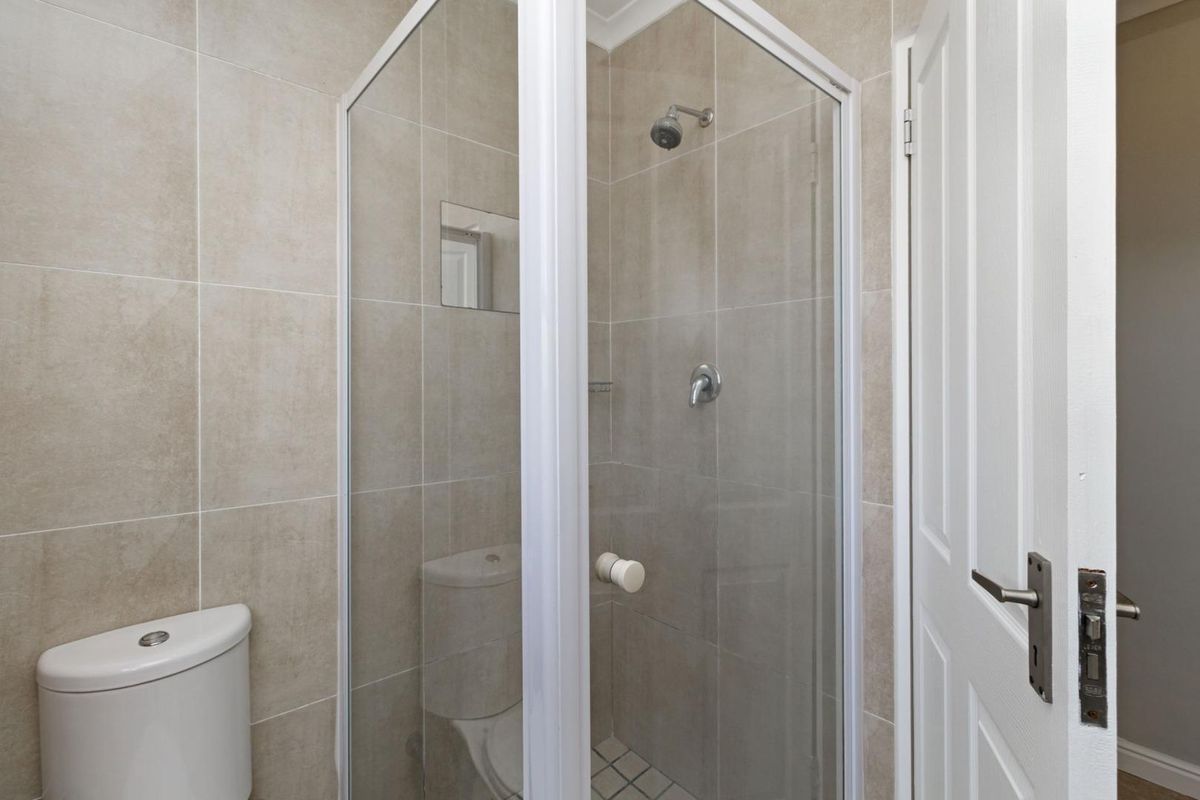 A clean and functional bathroom featuring a glass-enclosed shower, modern toilet, and neutral wall tiling.
