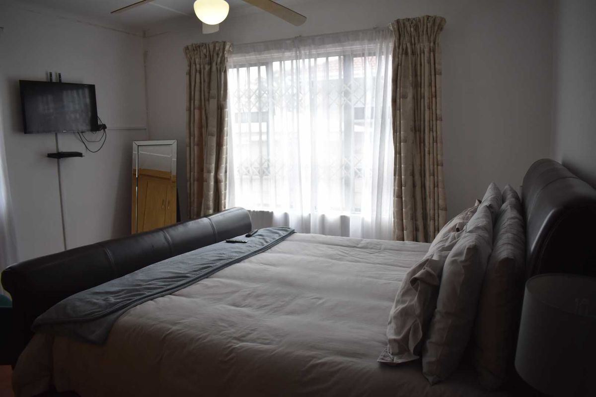 A bedroom featuring a ceiling fan and a window with security bars, providing natural light.